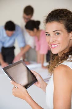 Portrait of beautiful businesswoman holding digital tablet with collaegues working in background at office