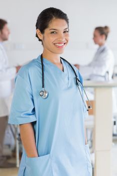 Portrait of smiling female nurse with doctors in background at hospital