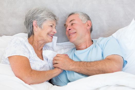 Romantic senior couple holding hands in bed at home