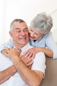 Loving senior woman embracing husband sitting on sofa at home