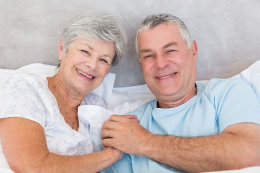 Portrait of happy senior couple holding hands in bed at home