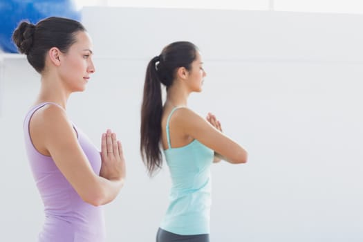 Side view of beautiful young sporty women with joined hands in fitness studio