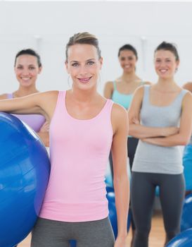 Portrait of an instructor holding exercise ball with fitness class in background at fitness studio