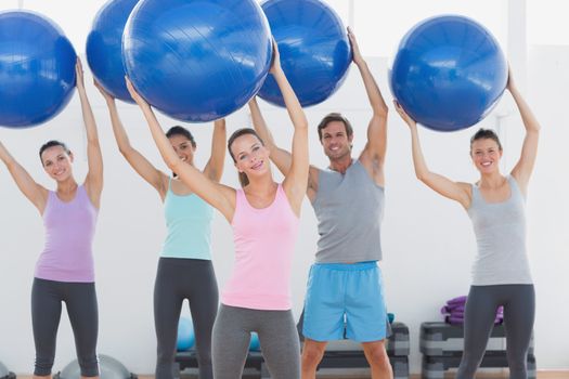 Portrait of an instructor and fitness class holding up exercise balls at the fitness studio