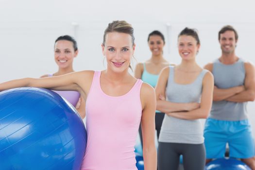 Portrait of an instructor holding exercise ball with fitness class in background at fitness studio