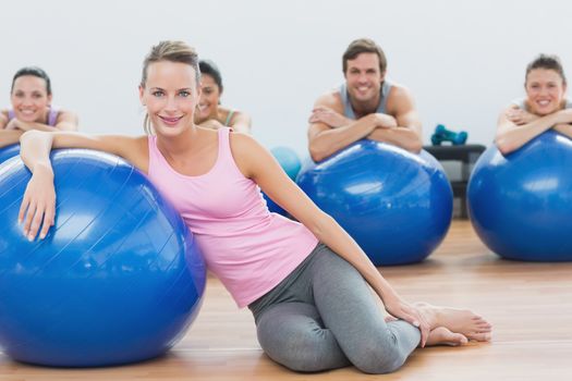 Portrait of an instructor and fitness class with exercise balls sitting at fitness studio