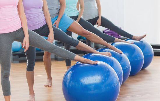 Low section of instructor and fitness class with exercise balls at fitness studio