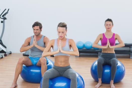 Sporty young people with joined hands sitting on exercise balls in the gym