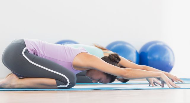 Side view of two sporty young women in meditation pose at fitness studio