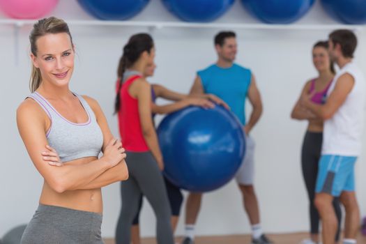 Portrait of a fit smiling young woman with friends in background at fitness studio