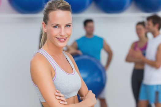 Portrait of a fit smiling young woman with friends in background at fitness studio