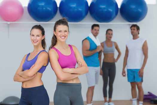 Portrait of fit young women in sports bra with friends in background in fitness studio