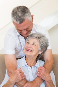 Senior man hugging wife sitting on sofa at home