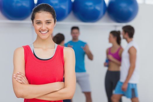 Portrait of a fit smiling young woman with friends in background at fitness studio