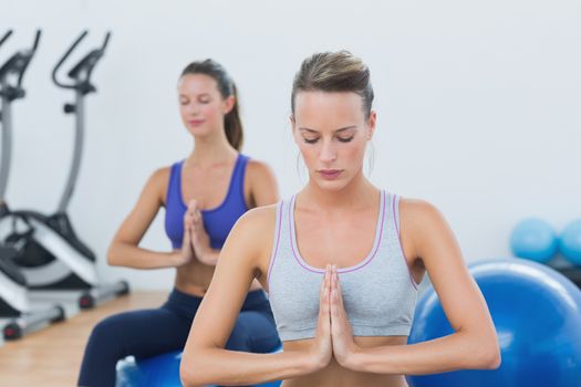 Sporty young women with joined hands and eyes closed on exercise balls in the gym