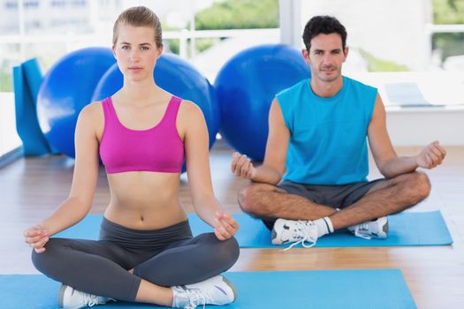 Full length portrait of a young couple sitting in lotus posture at fitness studio