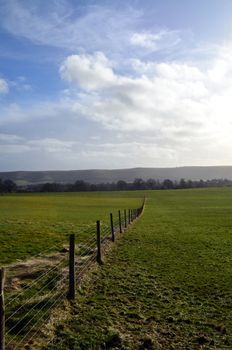 Wire fence running through open fields in Sussex,England.The South Downs hills are in the distance.