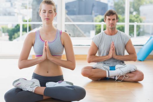 Sporty young couple in meditation pose with eyes closed at fitness studio
