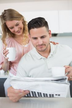 Young couple reading newspaper while holding coffee mugs in kitchen