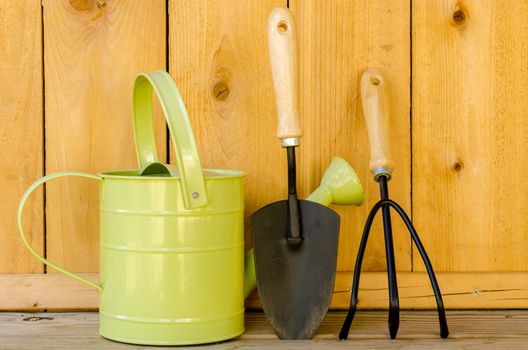 Gardening tools with watering can, trowel, and hand cultivator on wood background.