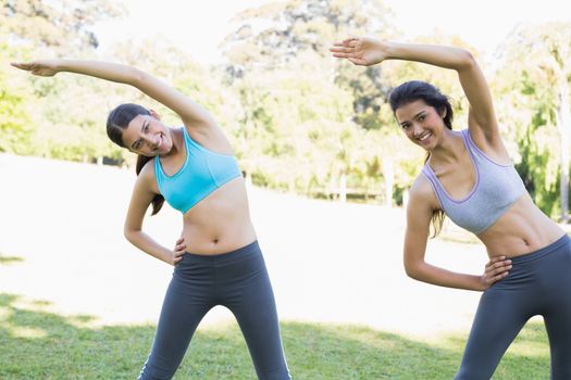 Portrait of smiling sporty women stretching in park