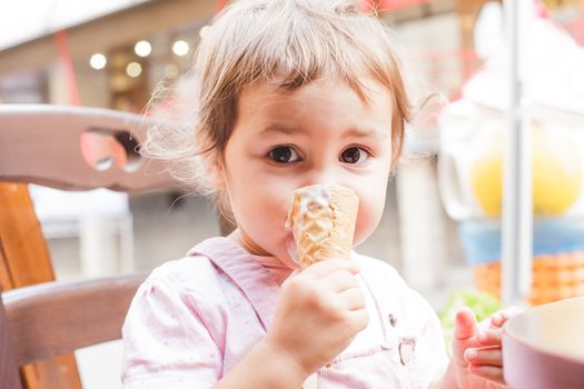 Loverly little girl eats an ice cream in cafe outdoor