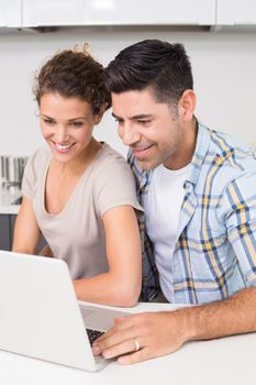 Smiling couple using laptop together at home in kitchen