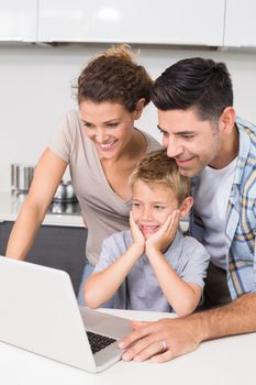 Parents using laptop with their son at home in kitchen