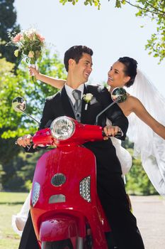 Portrait of a newlywed couple sitting on scooter in the park