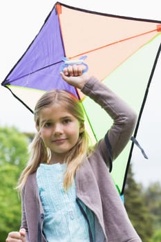 Portrait of a cute young girl with a kite standing outdoors