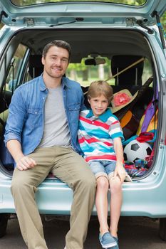 Portrait of a happy father and son sitting in car trunk while on picnic