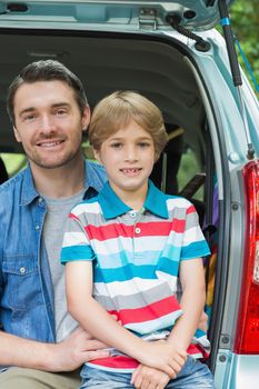 Portrait of a happy father and son sitting in car trunk while on picnic