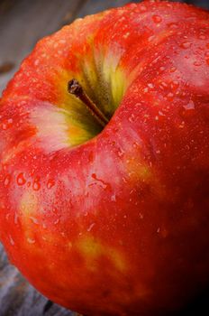 Delicious Red Apple and Stem Covered with Water Droplets closeup on Wooden background