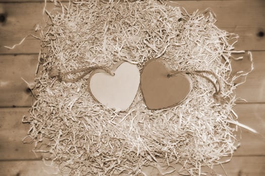 two wooden hearts in a love nest made of straw on a wooden background in sepia