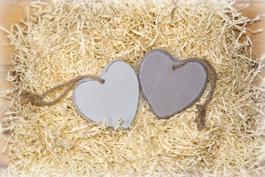 two wooden hearts in a love nest made of straw on a wooden background