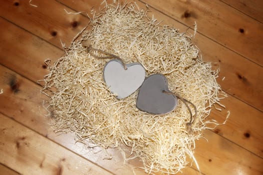 two wooden hearts in a love nest made of straw on a wooden background