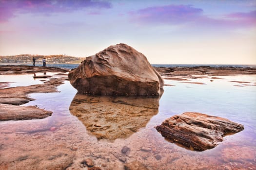 South Avoca Rocks, late afternoon sunset  Australia.  Larger rocks sit in a large still rockpool at low tide.This is a bracketed shot hdr   People in background have been blurred for obscurity.