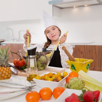 Blond kind girl junior chef on countertop preparing salad