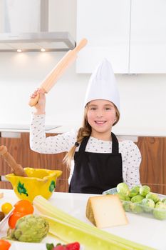 Blond kid girl junior chef on countertop funny gesture with roller knead