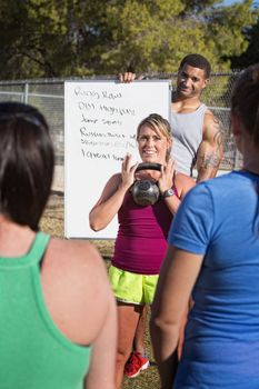 Smiling fitness instructors demonstrating weight lifting to a class