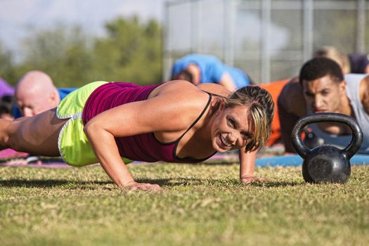 Embarrassed woman doing push-ups with group outdoors