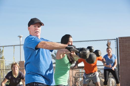 Mature male lifting kettle bell weights in outdoor class