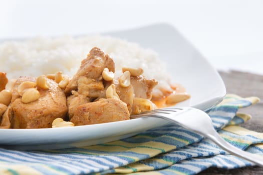 Plate of diced meat fried in batter and served with peanuts and boiled rice on a striped cloth with a silver fork for a tasty dinner, close up view