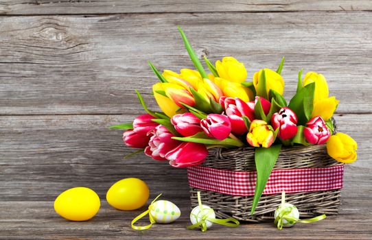 spring tulips in wooden basket with Easter eggs, on wooden background