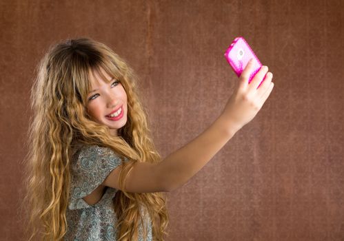 Blond kid girl taking pictures with mobile smartphone portrait on vintage background