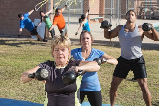 Mature woman and group exercising in outdoor boot camp fitness class