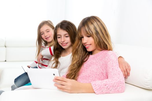 three kid sister friends girls group playing together with tablet pc on white sofa