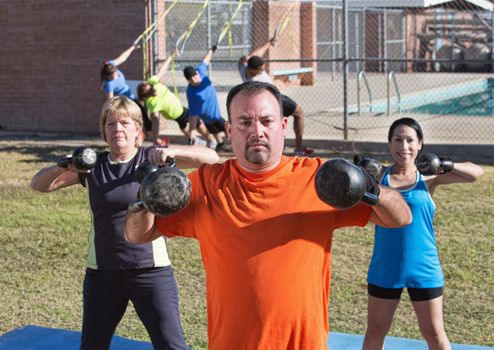Three adults exercising shoulder muscles with kettle bell weights