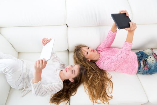 Children friends kid girls having fun playing with tablet pc lying on white sofa