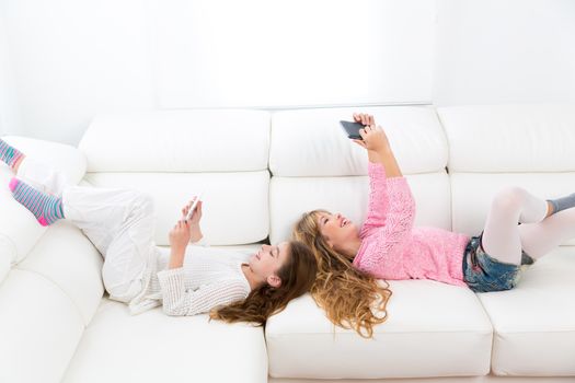 Children friends kid girls having fun playing with tablet pc lying on white sofa